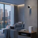 Smart home devices in a Dubai apartment: a wall-mounted IP security camera, a keypad smart door lock, and a Wi-Fi router, with Dubai Marina towers through the window