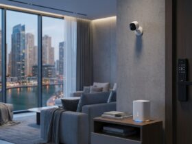 Smart home devices in a Dubai apartment: a wall-mounted IP security camera, a keypad smart door lock, and a Wi-Fi router, with Dubai Marina towers through the window